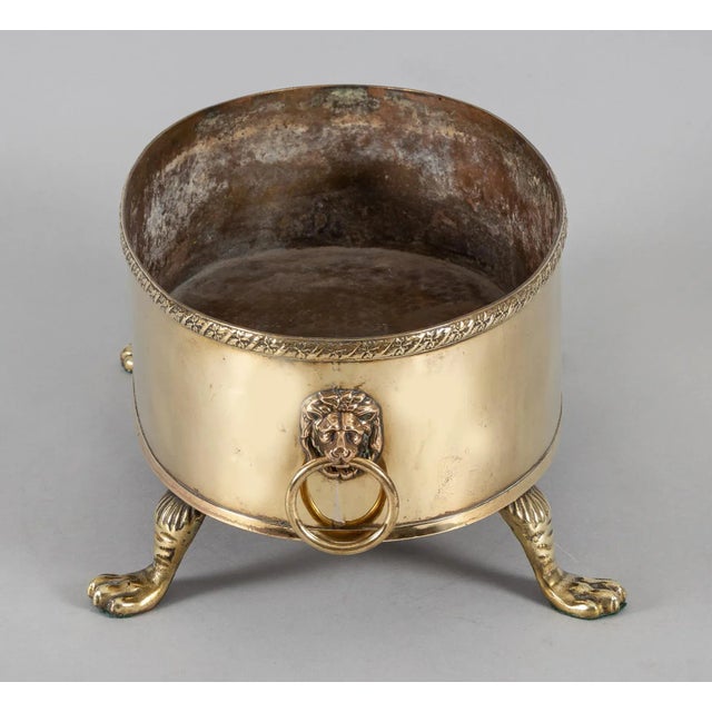 Antique oval brass jardiniere or wine cooler with a decorative border rim at the top, lion’s masks handles at the sides,...