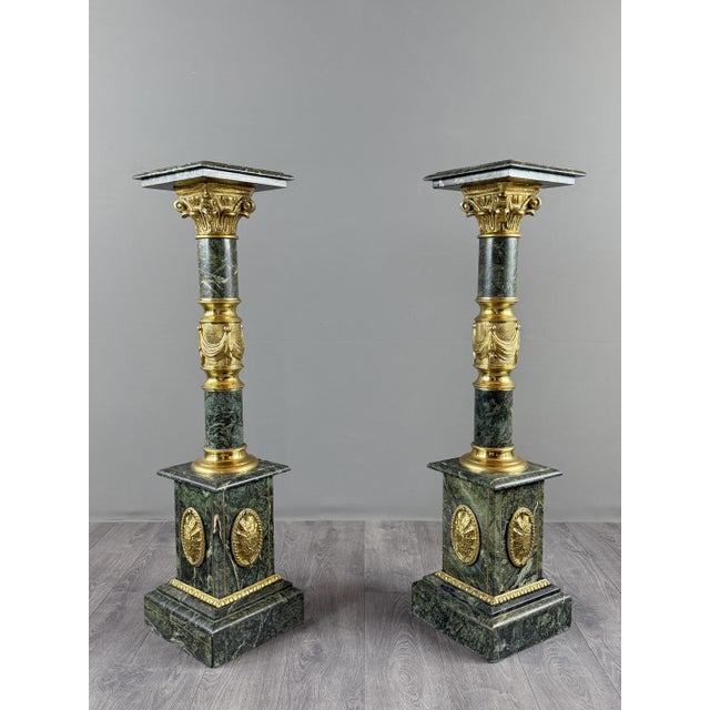 An elegant pair of decorative columns in veined green marble, richly adorned with gilt bronze and brass elements. the...
