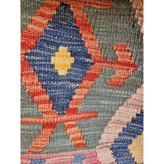 A striking vintage Afghan kilim, handcrafted in wool, featuring a rich tribal geometric design and a sophisticated color...