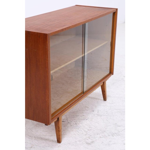 Vintage chest of drawers with delicate glass sliding doors and a slim base. The combination of open storage space and a...