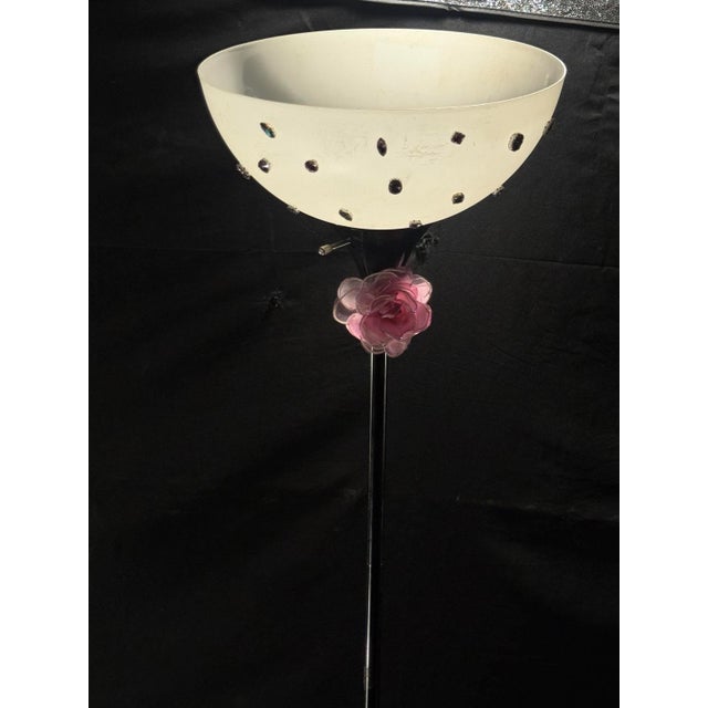 Torchiere floor lamp with a slender black frame, round weighted base, a pink floral accent and an upward-facing frosted...