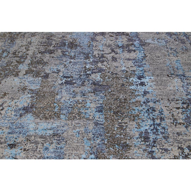 This Indian wool and silk blend rug features a gray field with an abstract pattern detailing blue colors. Its composed...