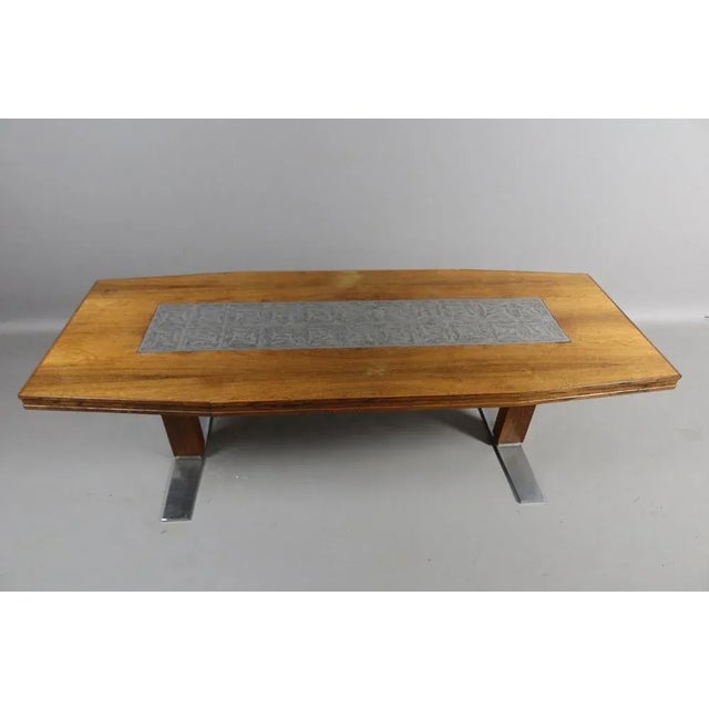 Slightly oval coffee table in rosewood. The tray is decorated with a engraved metal plate and rests on two finished wooden...
