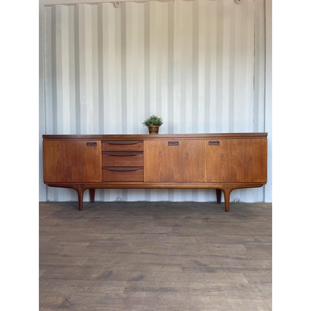 This large mid-century teak sideboard by greaves & thomas exemplifies the elegance and functionality of british modernist...