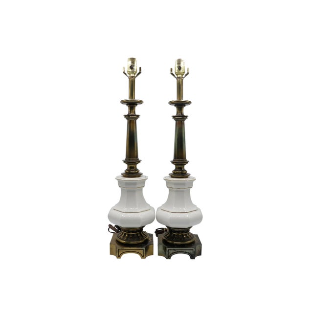 A pair of French Empire style table lamps made by Stiffel. Brass columns are turned with large ceramic fonts in white...