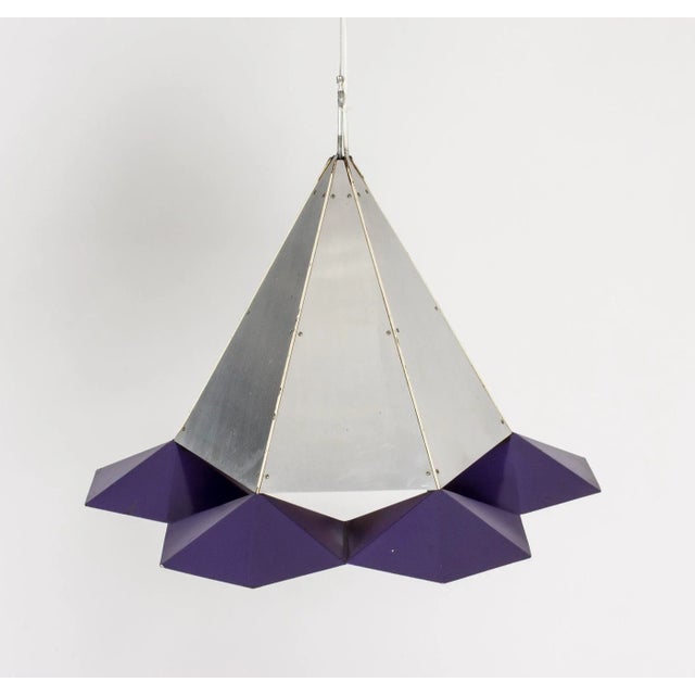 This pendant lamp is in a style reminiscent of Simon Henningsen. The conical body is made from brushed steel and the base...