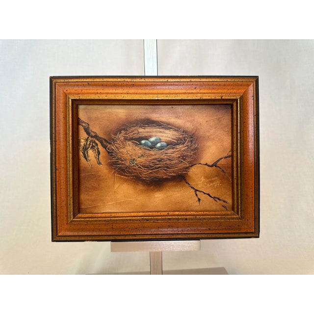 This 1975 vintage oil depicts a singular bird nest with a trio of eggs in robins egg blue on a singular branch. This light...