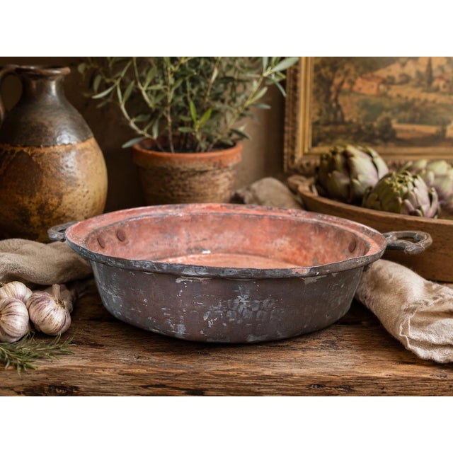 A beautifully aged vintage copper-tone serving pan featuring sculptural brass-toned side handles and a richly weathered...