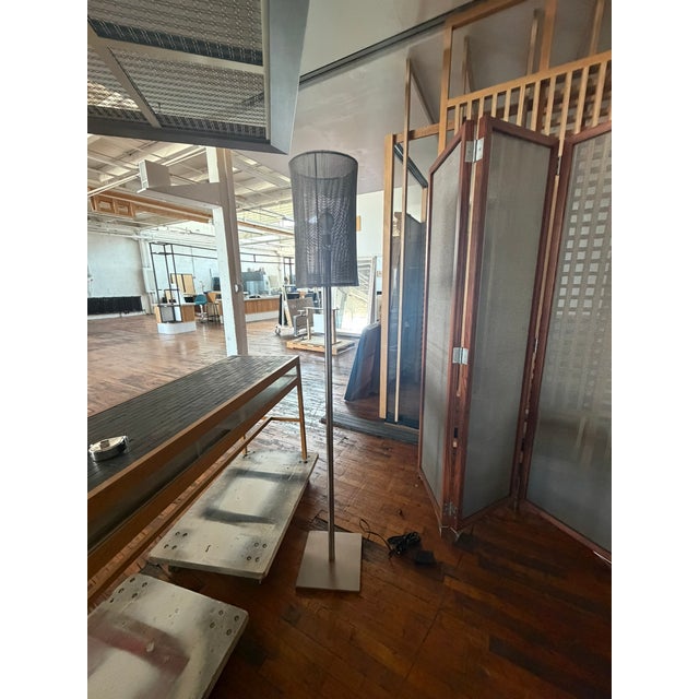 This custom steel mesh floor lamp showcases a tall cylindrical shade crafted from layered perforated steel, producing a...