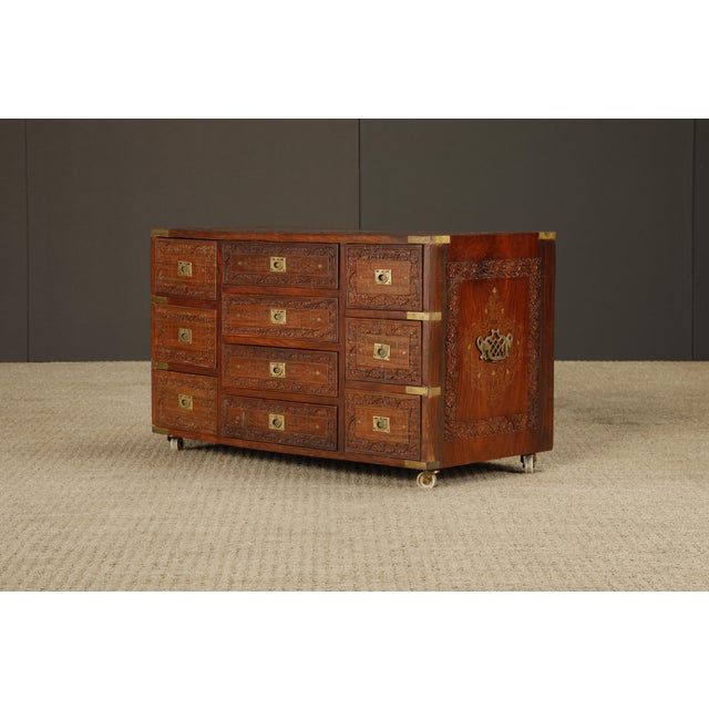 Striking vintage dresser or chest featuring intricate carved wood and brass inlay detailing throughout. The piece is...