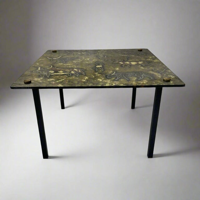 A Modernist eglomisé glass top side table. Painted glass top with cave painting motif , resting on a black iron frame....