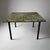 A Modernist eglomisé glass top side table. Painted glass top with cave painting motif , resting on a black iron frame....