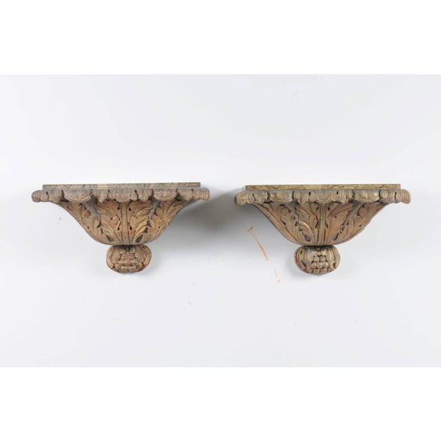 A pair of Italian richly carved giltwood wall brackets rom the second half of the 19th century with faux-marble painted...