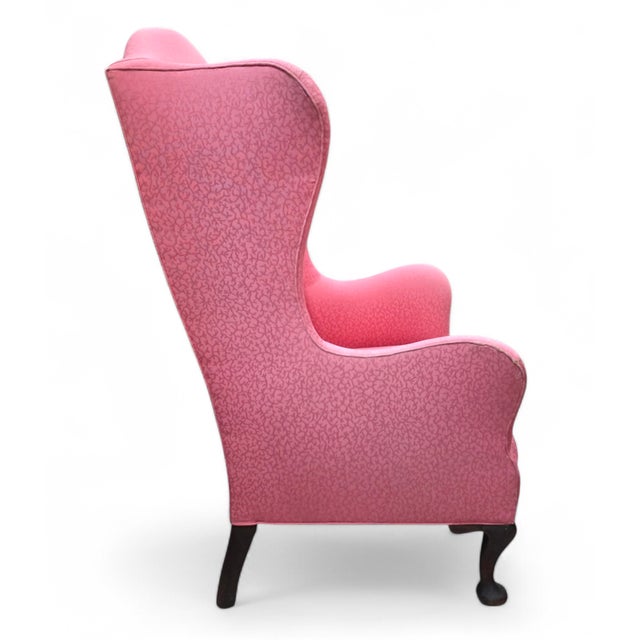 This 19th-Century wingback armchair is a classical seating piece upholstered in a richly toned rose-pink patterned fabric....