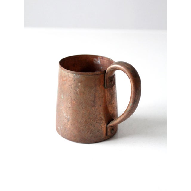 A vintage copper mug with a gently tapered form, rolled rim, and substantial riveted loop handle. The warm copper surface...