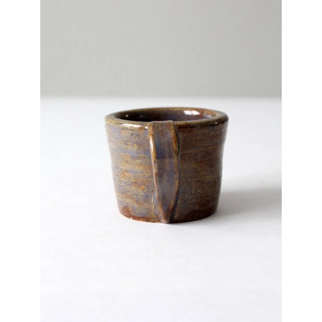 This is a vintage studio pottery mug. Signed by the artist, the handmade mug has a warm glaze of russet, taupe, and...