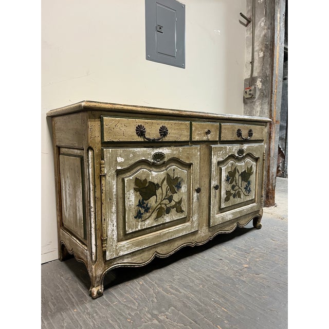 French Provincial style sideboard featuring a distressed painted finish and decorative floral panels. Two cabinet doors...