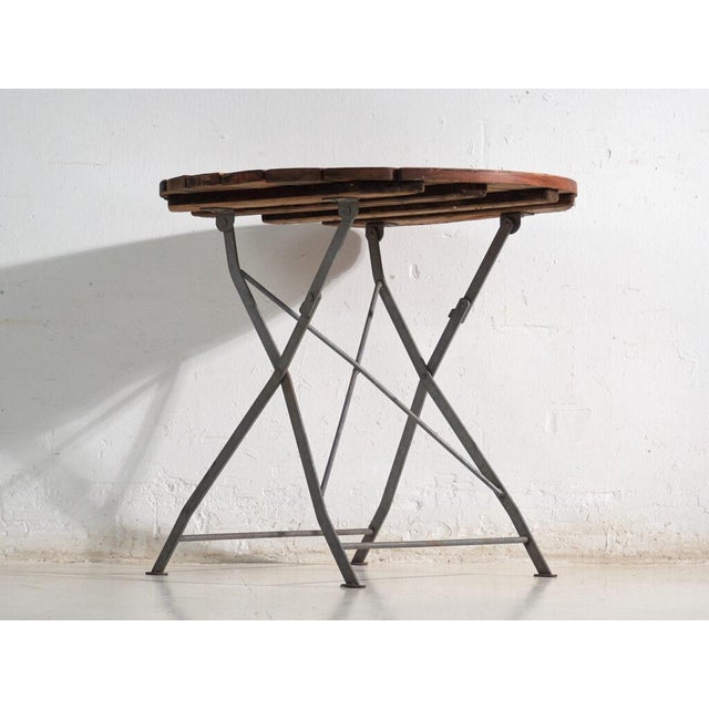 This antique folding garden table in wood and iron is a bistro table with a round slatted top and a folding iron base. It...