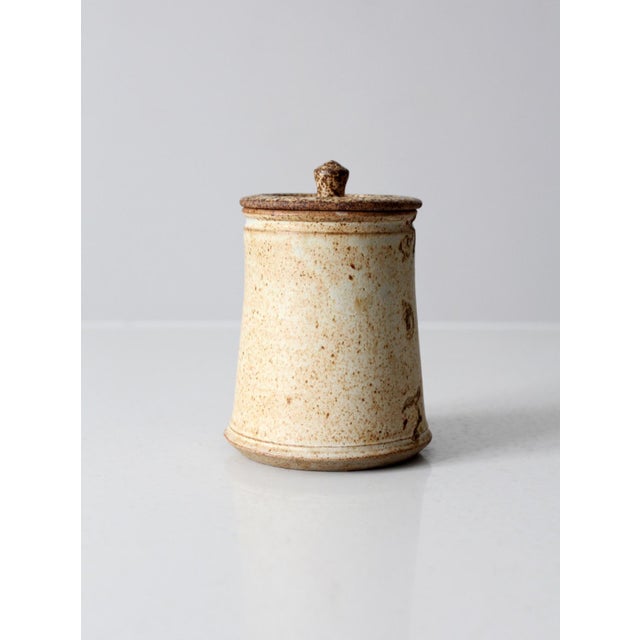 This vintage studio pottery jar features an earthy speckled tan glaze with etched detailing on one side and a small...