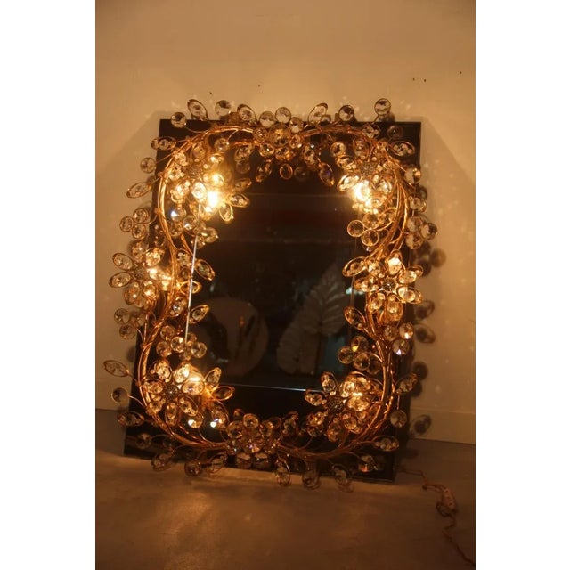 This mirror with a gilded brass structure and embedded crystals is illuminated through light bulbs and is reminiscent of...
