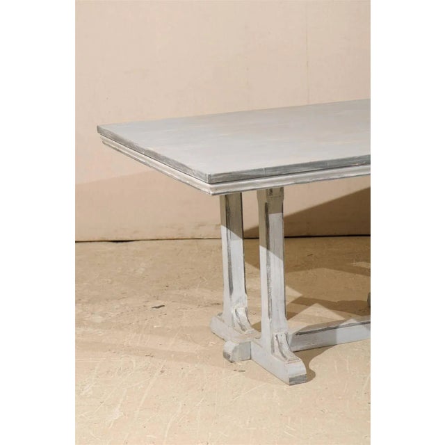 A large European grey painted wood rectangular dining table. This dining table features an old trestle base with cross...