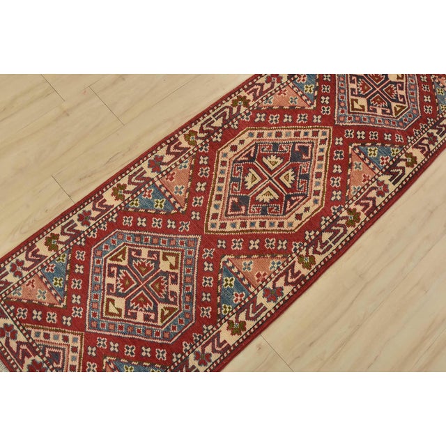 A tribal Caucasian Kazak runner hand-knotted with fine wool on a cotton foundation. This rug features geometric medallions...