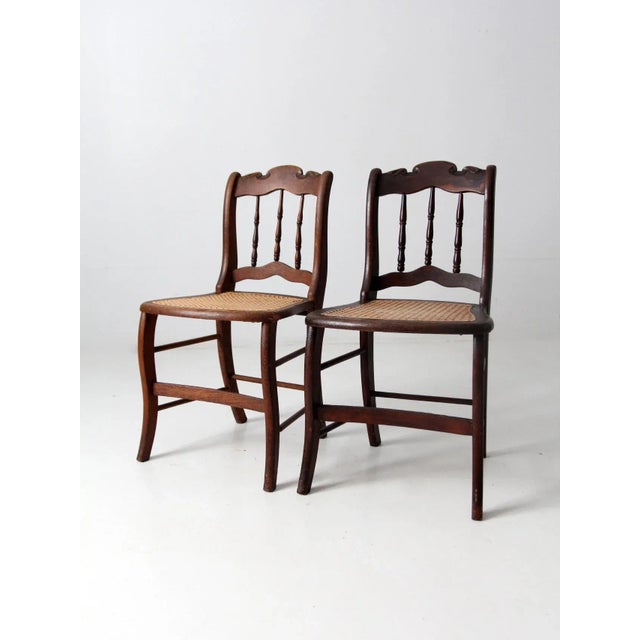 This is a pair of antique wooden side chairs. The wood chairs feature elegant bannister backs with decoratively shaped...