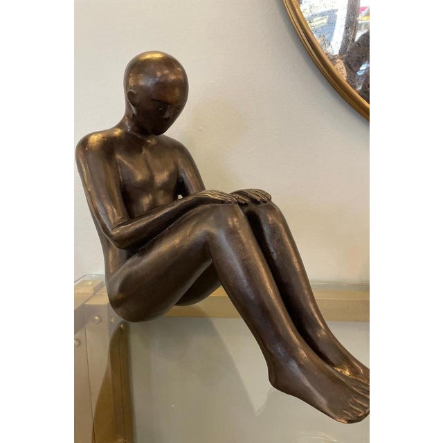 Bronze sculpture by Mimmo Paladino depicting a human figure crouching on the ground. The sculpture is highly expressive,...