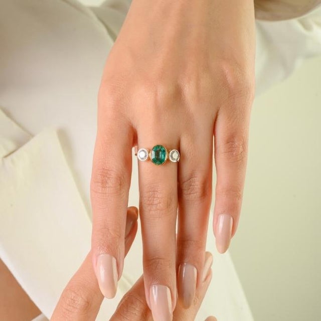 This elegant three-stone ring features 1 oval cut natural zambian emerald totaling 1 carat, set in rich 18k yellow gold....