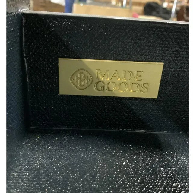 A two tier black linen console table with two drawers and a lower shelf with brass caps to feet and brass hardware on...