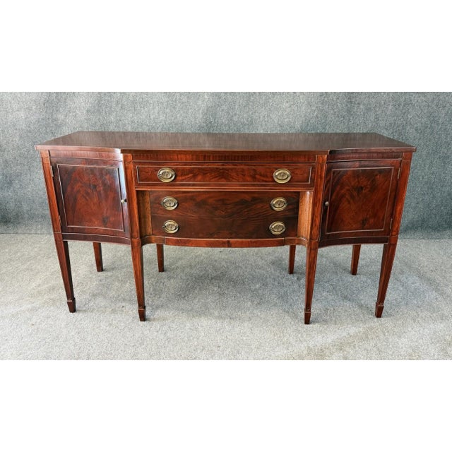 This vintage flamed mahogany sideboard features beautifully figured veneer panels, a gently bowed center drawer stack, and...