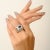 This bold 925 sterling silver ring features an oval-cut blue stone at the center, framed by round-cut white cubic zirconia...