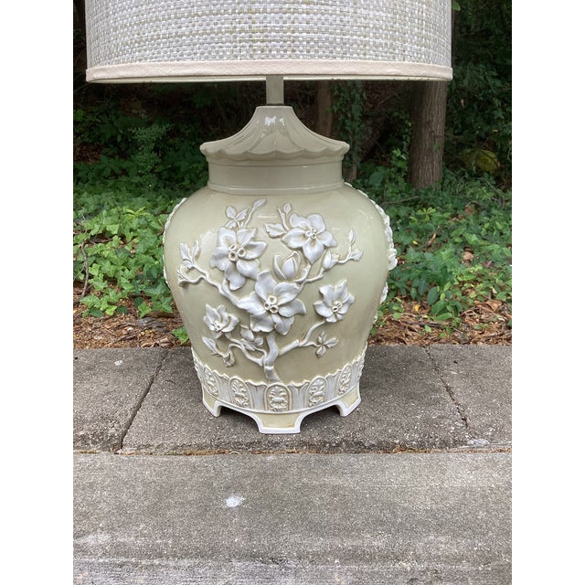 A beautifully sculptural chinoiserie-style porcelain table lamp featuring an elegant raised floral relief in a soft...
