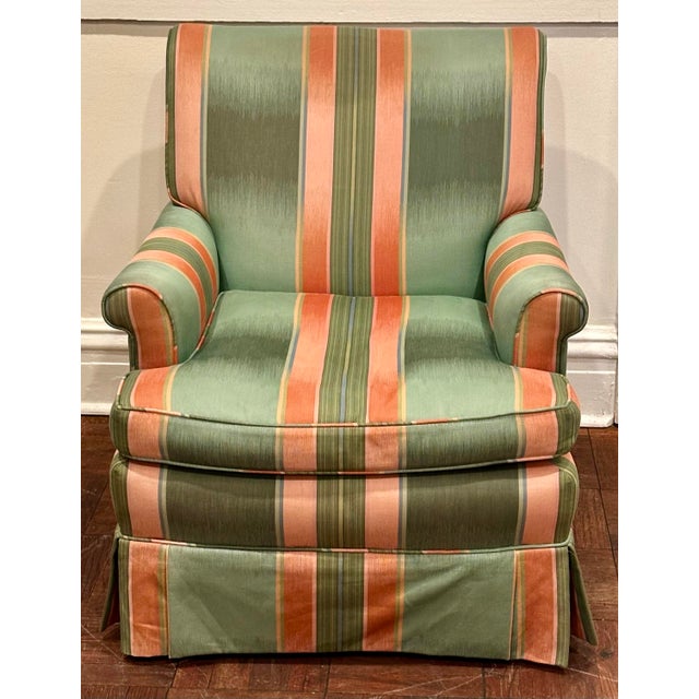 A generously proportioned upholstered club chair in a striking striped textile of soft green, coral and muted gold. The...