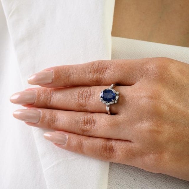 This elegant halo engagemnt ring features 1 natural oval-cut deep blue sapphire totaling 2 carats, set in rich 14k white...