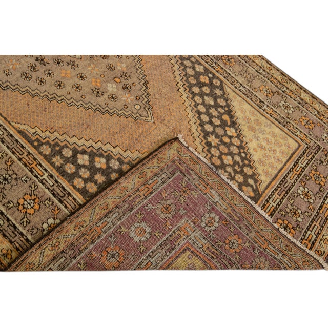 Beautiful antique Khotan hand-knotted wool rug with a tan field. This Khotan rug has a brown and orange accent in an all-...