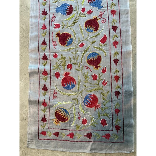 Hand-embroidered Suzani table runner from Uzbekistan — red and blue pomegranates on a golden vine over an ivory silk...