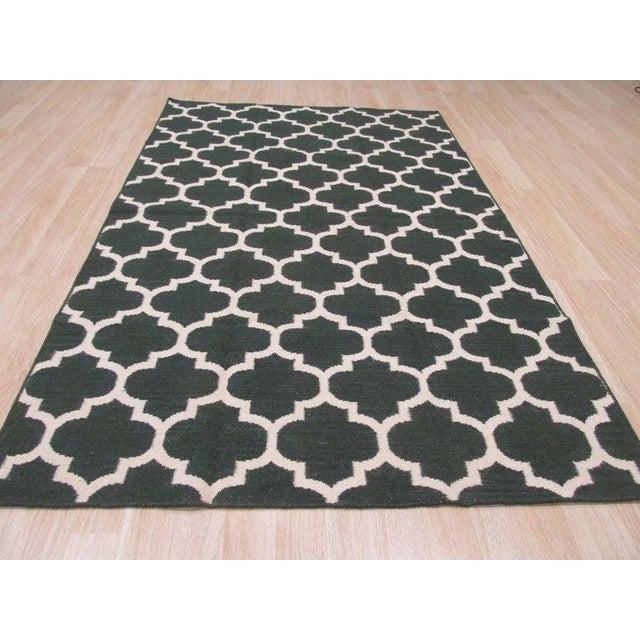 This green wool rug features a flat weave construction typical of the Kilim style. It serves as a substantial floor...