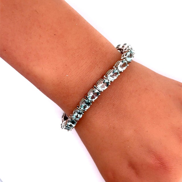 A contemporary tennis bracelet, showcasing a sleek and elegant design. The bracelet is adorned with oval-cut aquamarines...