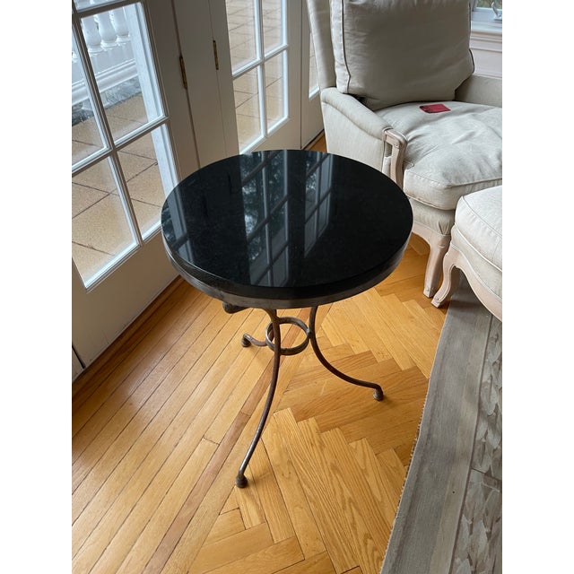 A small, French Maison Jansen style gueridon side table with a black marble top and circular tripodal pedestal iron base....