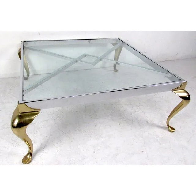 Vintage-modern coffee table featuring glass top with sculpted frame and legs, brass finish on legs. Dimensions: 39w 39d...
