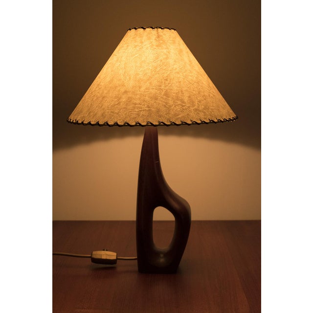 Beautifully shaped vintage table lamp made of teak with a beige lampshade. The shade has beautiful leather details on the...