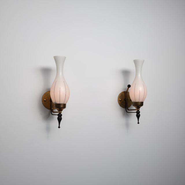 A pair of italian wall sconces from the 1950s combining brass, black-lacquered metal and hand-blown opaline glass. The...