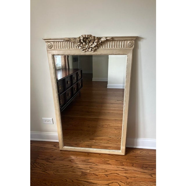 This elegant rectangular mirror features beveled glass, carved wood frame, gold gilt finish, bow and ribbon crest, and two...