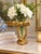 Elegant decorative vase featuring an oversized sculptural bow in a rich antiqued gold finish. The clear flared glass...