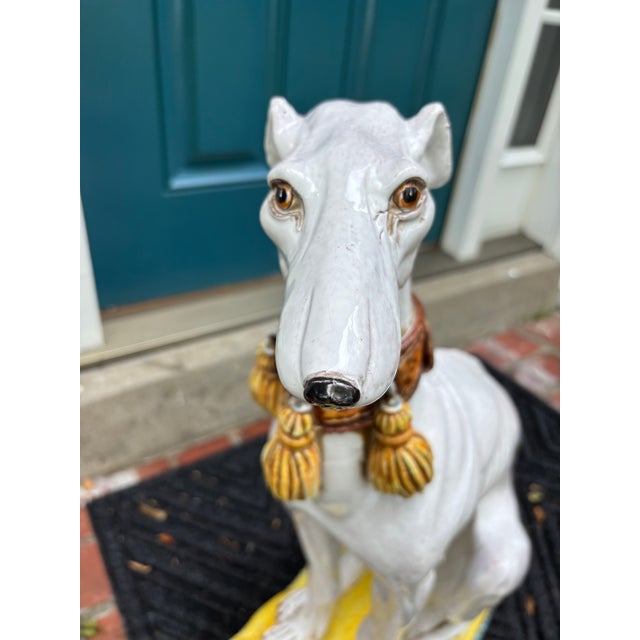 A large Italian glazed terra cotta whippet or greyhound, seated on a tasseled pillow, beautifully-detailed and realistic,...