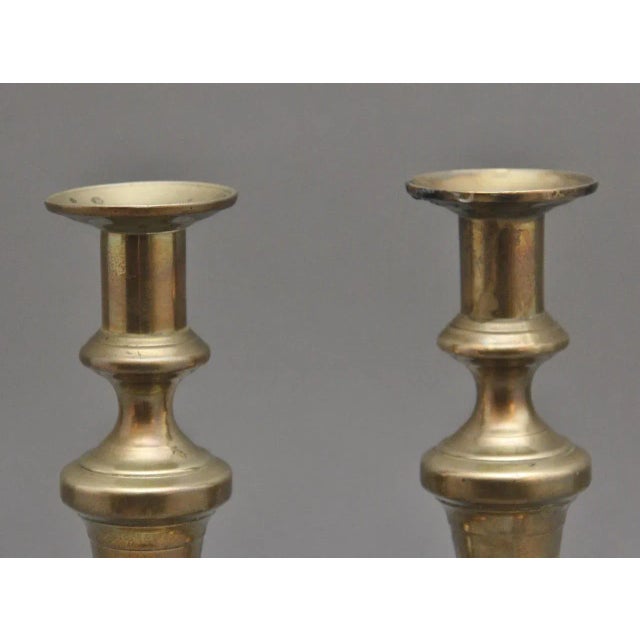 A pair of 19th Century brass candlesticks, having turned and shaped columns raised on a square platform base. Circa 1860.