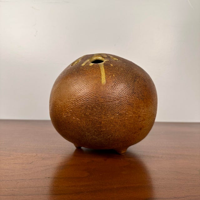 Sphere-shaped bud vase on three little feet. Bud vase has various sized holes along the top with dripped glaze detailing...