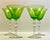 A set of four beautiful green cocktail glasses set atop a tassel shape fluted stem on a perfectly clear glass foot. An...