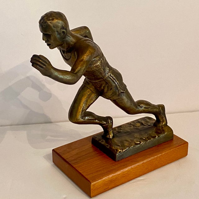 1950’s track and field trophy shows a male athlete in mid-stride leaning forward running with determination. It is made of...